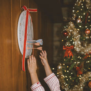 Kid grabbing magnetic darts off dartboard hung on the wall, with a ribbon, next to the Christmas tree